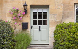 Light green front door surrounded by flowers and ornamental grasses