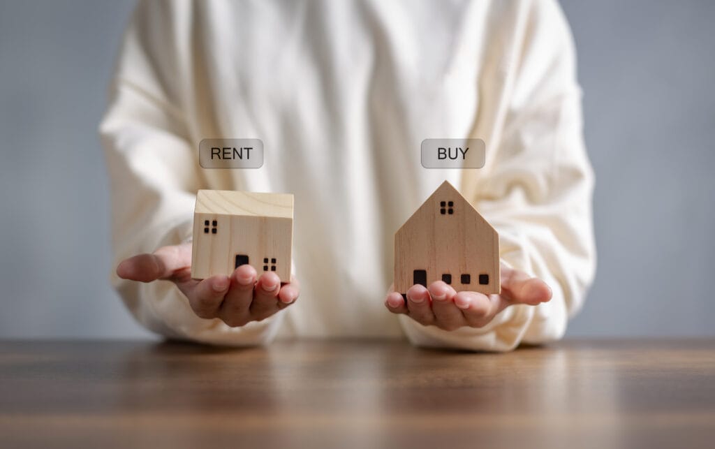 rent vs buy price to rent ratio image depicting person holding two buildings which represent an apartment for renting and a home for buying