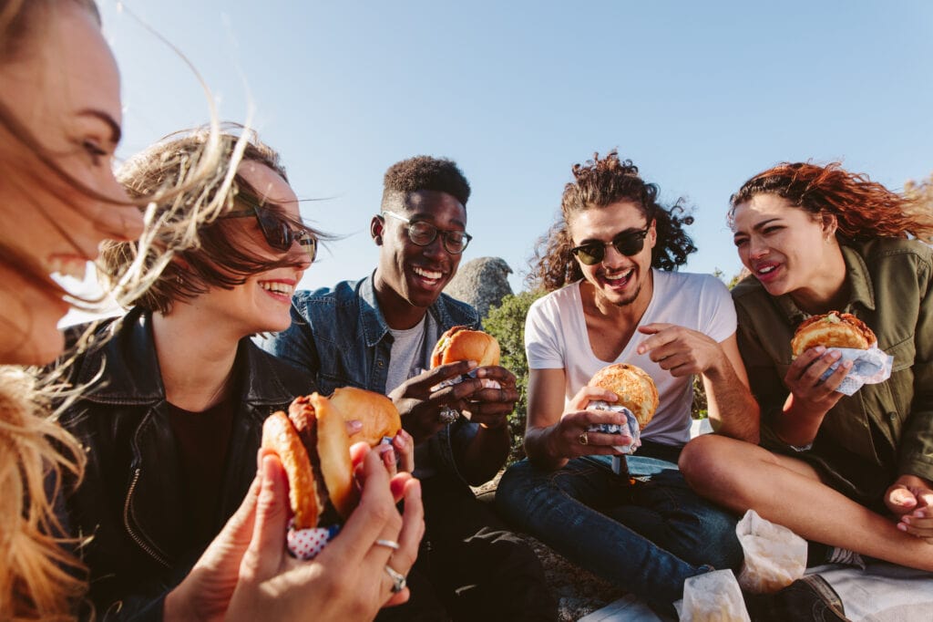 Young,People,Having,Summer,Picnic,And,Eating,Together,Sitting,On, Burgers near me, American burgers, best burger near me