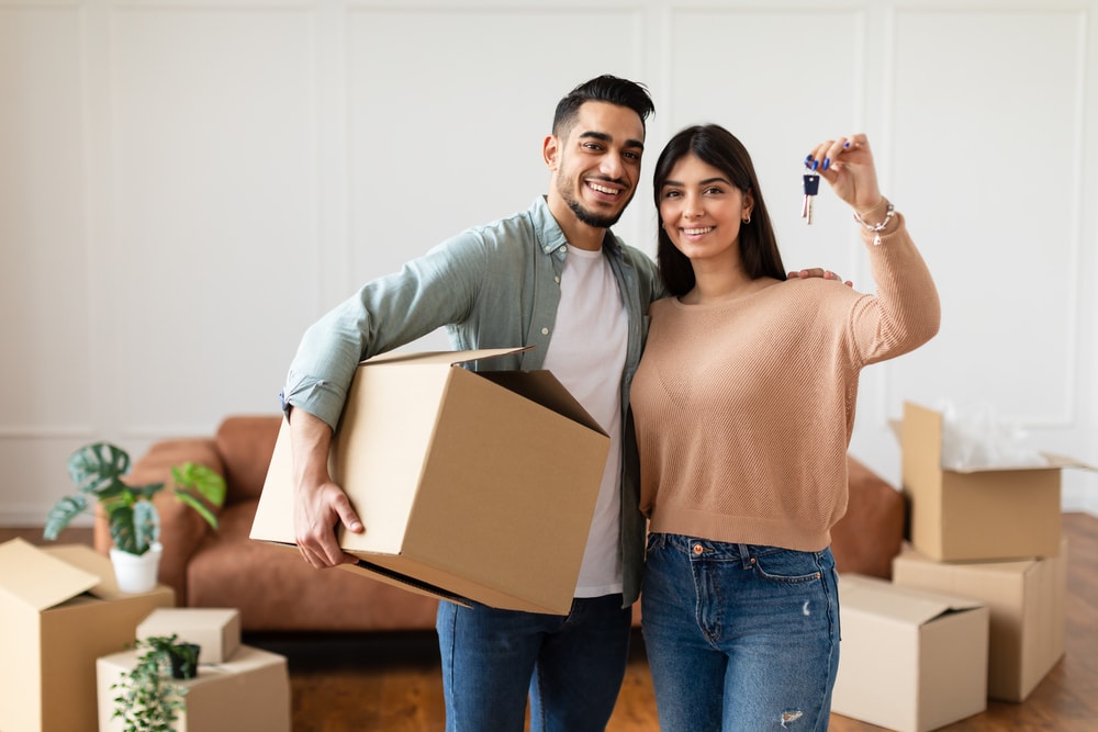 Cheerful Guy And Lady Hugging After Moving In New Apartment Standing In Living Room, why is renting better than buying, why is buying better than renting concept